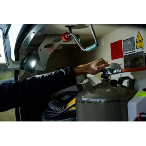 Oppladbar arbeidslampe LED SH 1000 MA i bruk, lyser opp hånd som justerer ventil på grå gassflaske i teknisk rom.