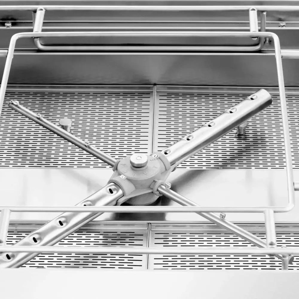 Rustfritt stålspylearm med hull, sett ovenfra på perforert rist i robust industriell oppvaskmaskin.