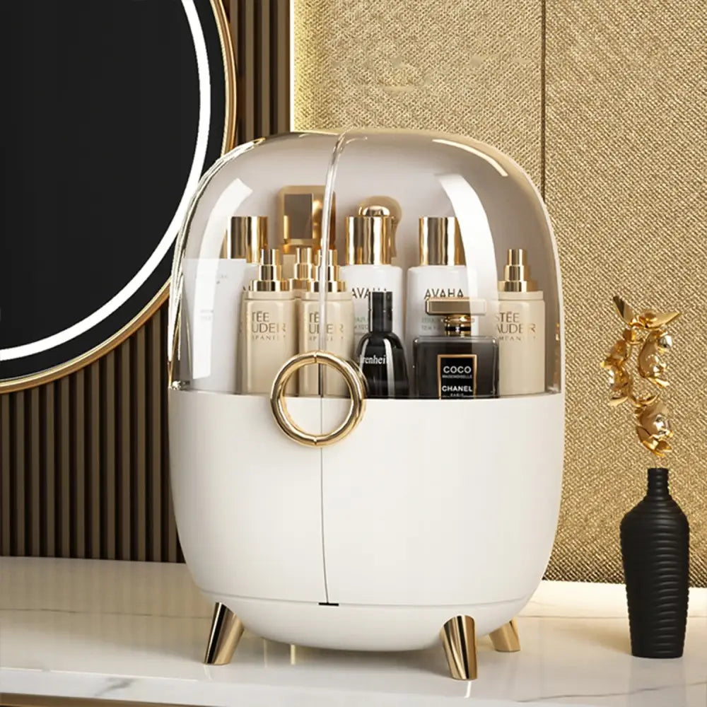 Organiser for kosmetikk og smykker, hvit oval boks med gjennomsiktig lokk og gulldetaljer, sett forfra.