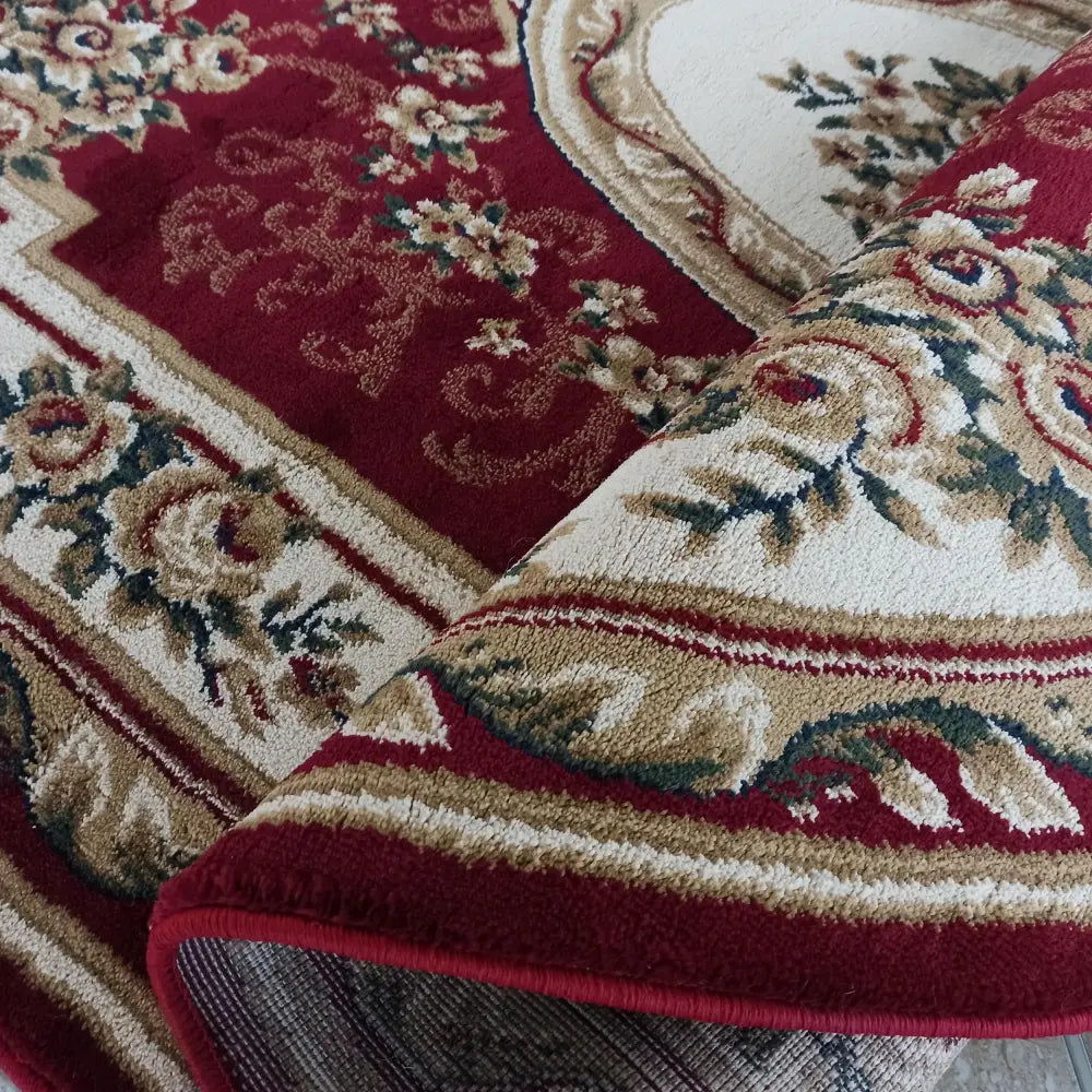 Ovalt teppesett i rødt med klassisk blomstermønster, detaljert nærbilde av tekstur og oppbrettet kant.