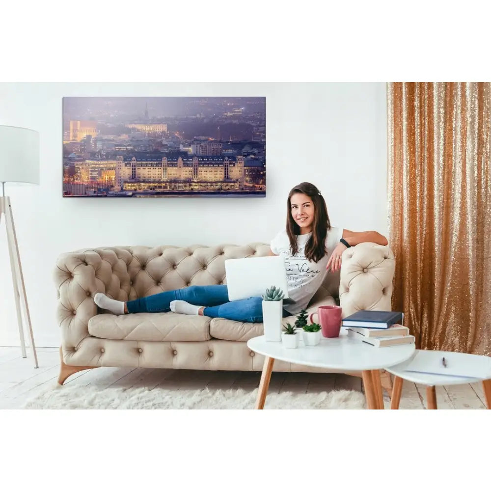 Panorama av Oslo lerretsbilde på veggen bak beige sofa, kvinne med laptop og hvitt bord i stuen.