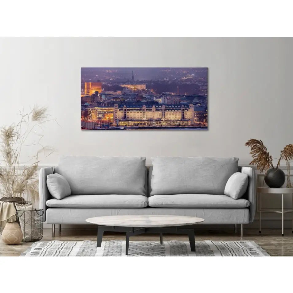 Panorama av Oslo på lerret, montert over lysgrå sofa med lyst trebord og tørkede planter i stueinteriør.