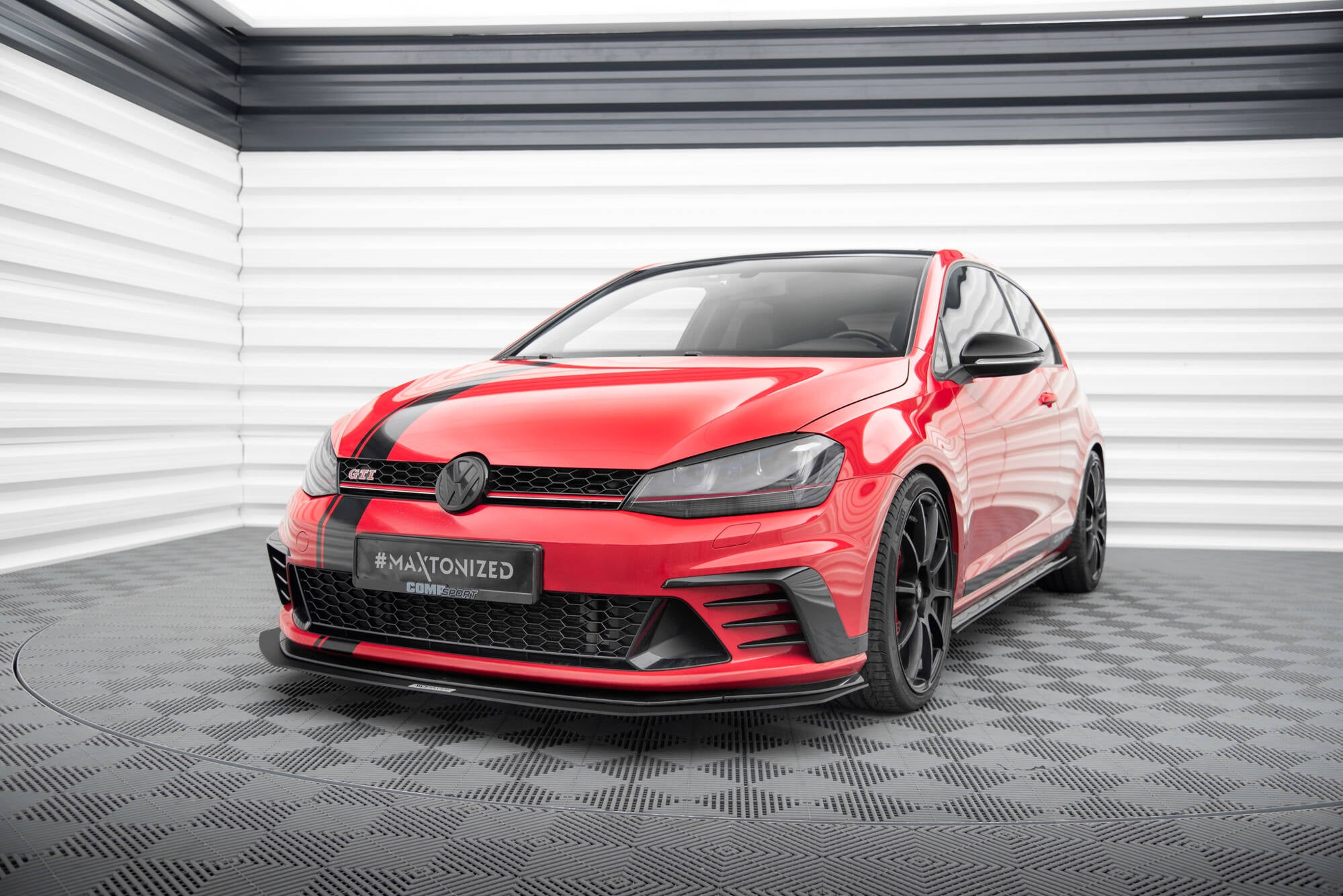 Spoiler på VW Golf VII GTI Clubsport, rød bil med svarte felger og panserstripe i lyst showroom.