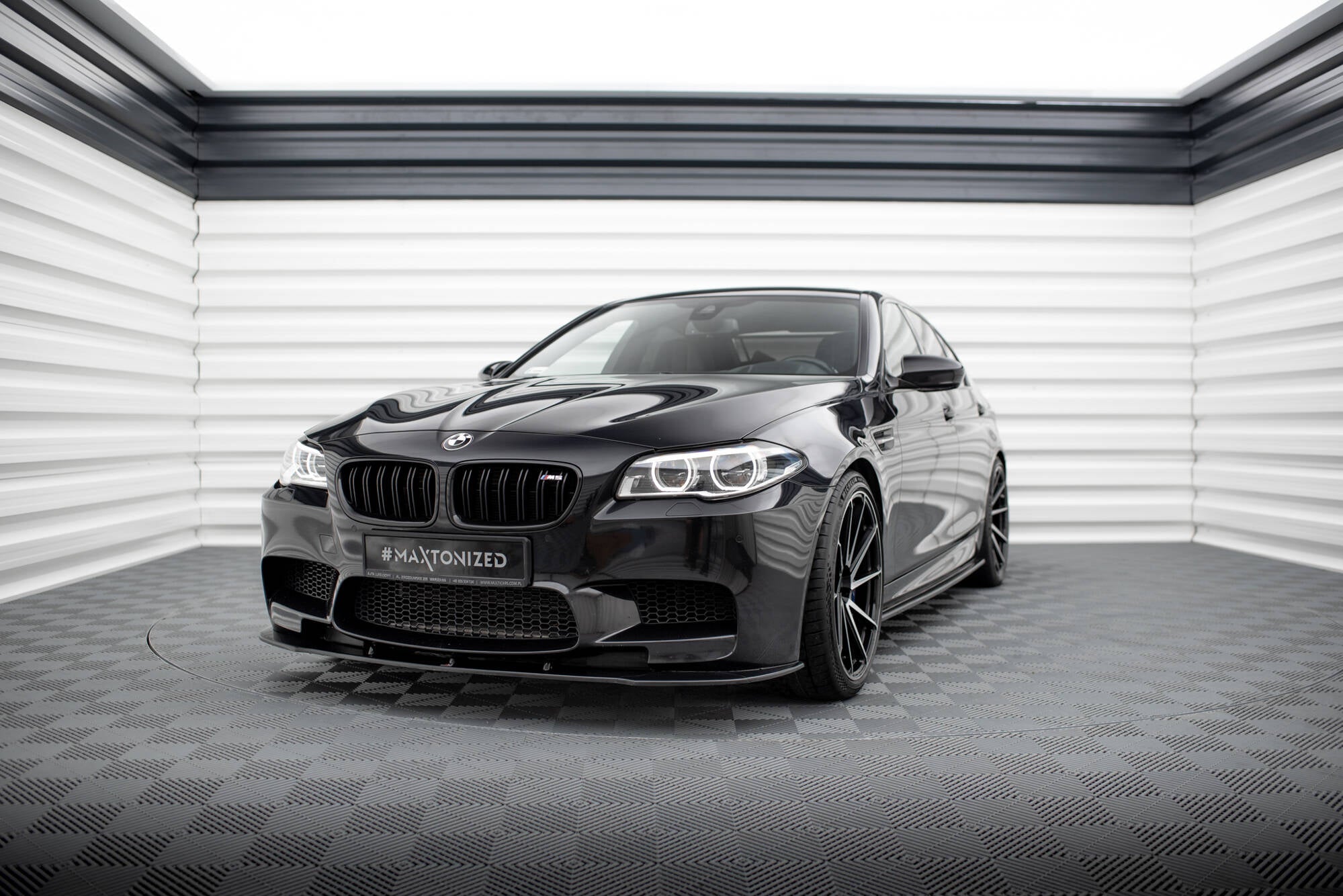 Frontspoiler BMW M5 F10 med store luftinntak, svarte felger og glanset finish sett forfra.