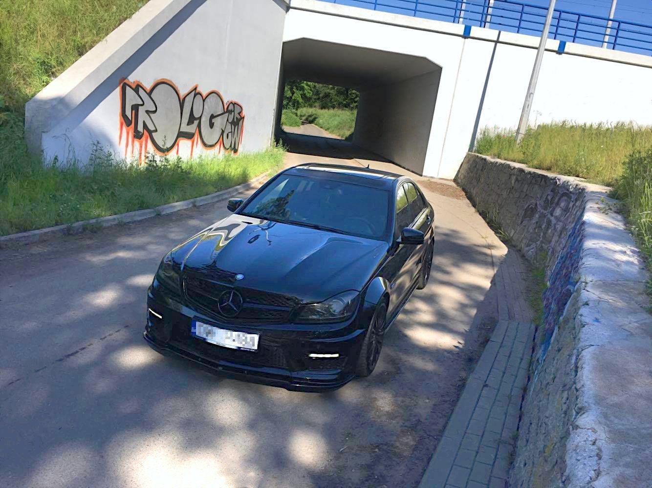 Front splitter på Mercedes C63 AMG W204, sort bil parkert under bro med graffiti på betongvegg.