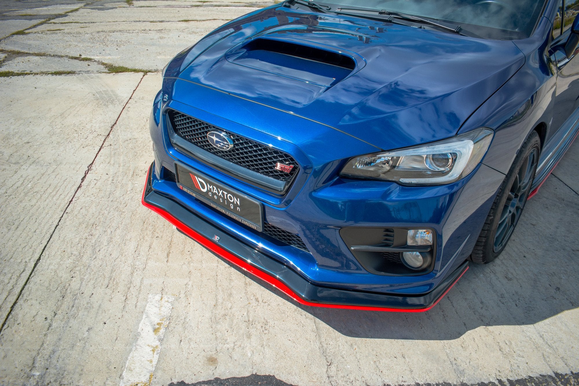 Frontspoiler Subaru WRX Sti ABS V.3 montert på blå bil med sort splitter og rød kant, sett forfra utendørs.