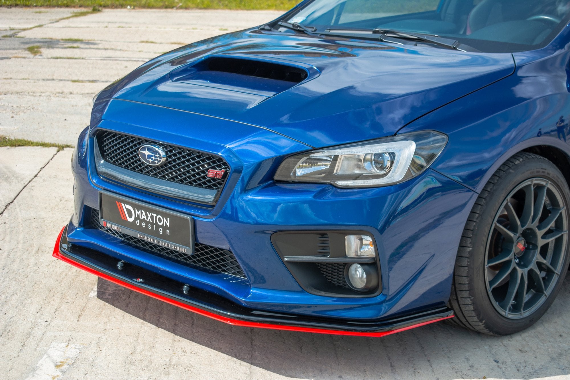 Frontspoiler Subaru WRX Sti V.4 i svart og rød plast på blå bil, sett fra skrå vinkel med felg og grill.