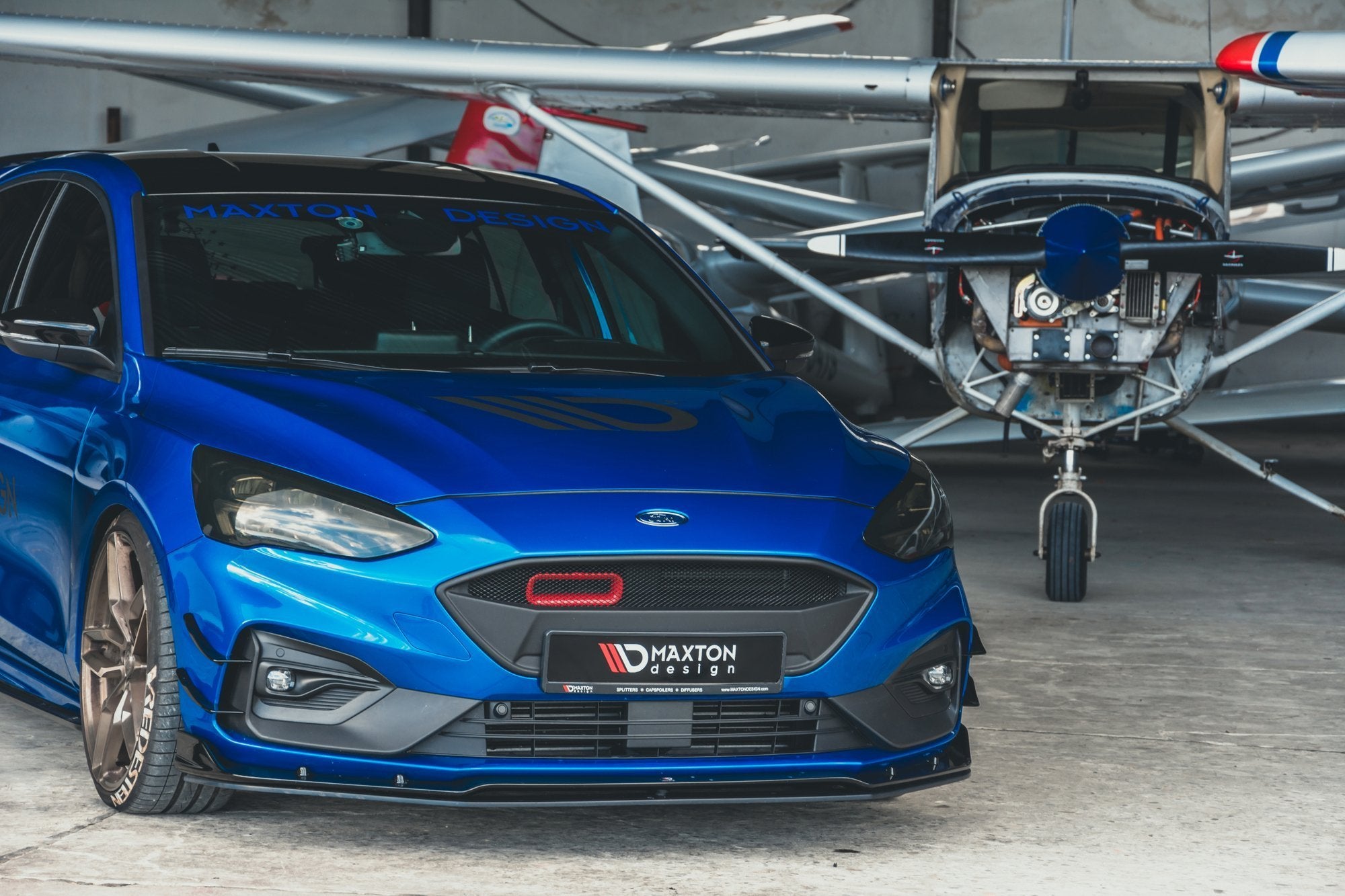 Frontspoiler på blå Ford Focus MK4 ST-Line med bronsefargede felger, sett forfra i garasje.