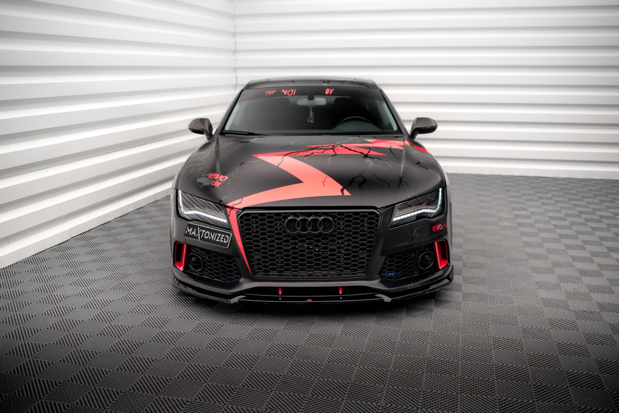 Frontleppe Audi A7 RS7 Look C7 montert på sort sportsbil med rød dekor, sett forfra i lyst rom.