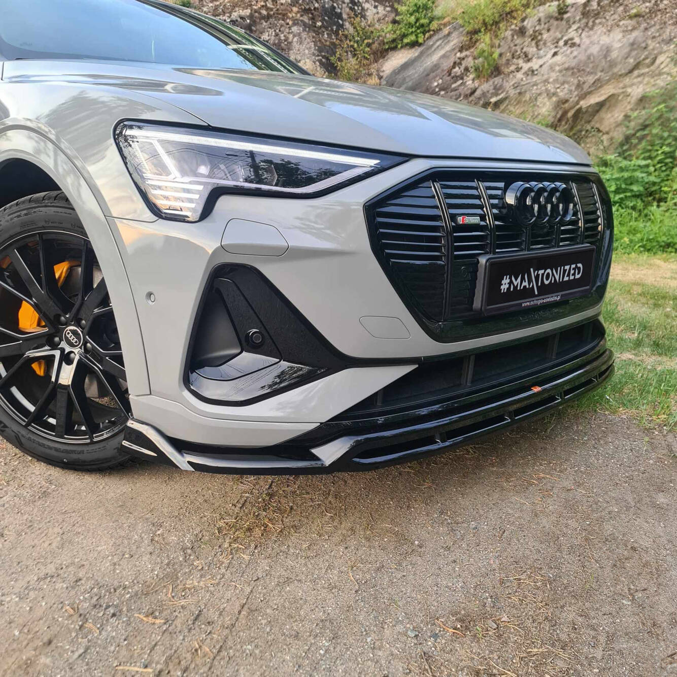 Front splitter på Audi E-Tron S-Line med sort grill, sorte detaljer og oransje bremsekaliper utendørs.