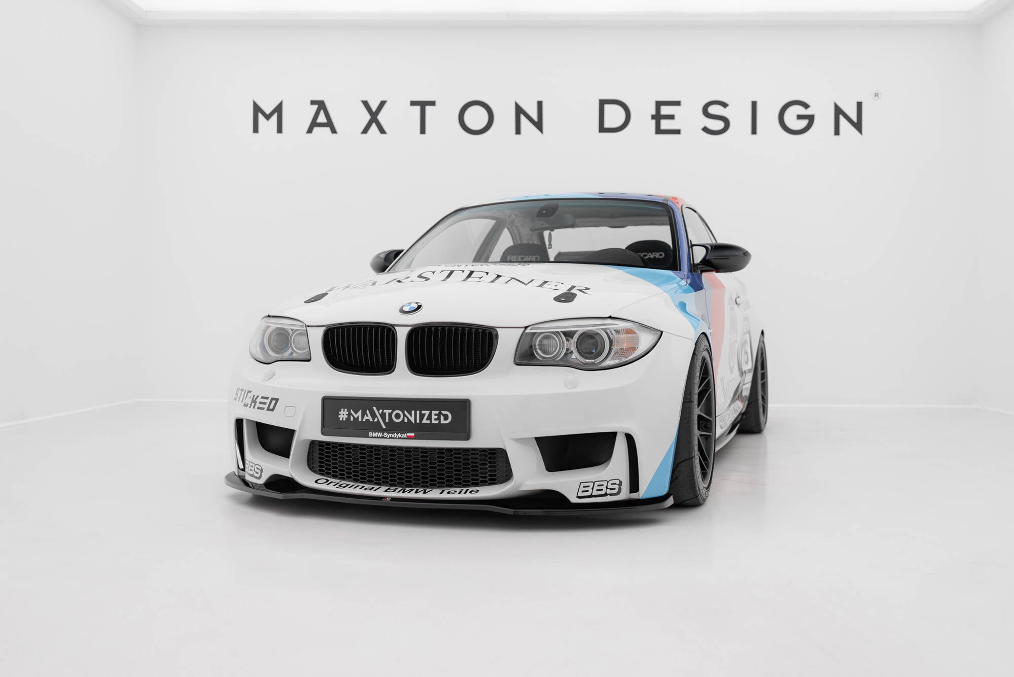 Frontspoiler på BMW 1 M Coupe E82 hvit sportsbil med svarte detaljer og racing-dekor i lyst studio.