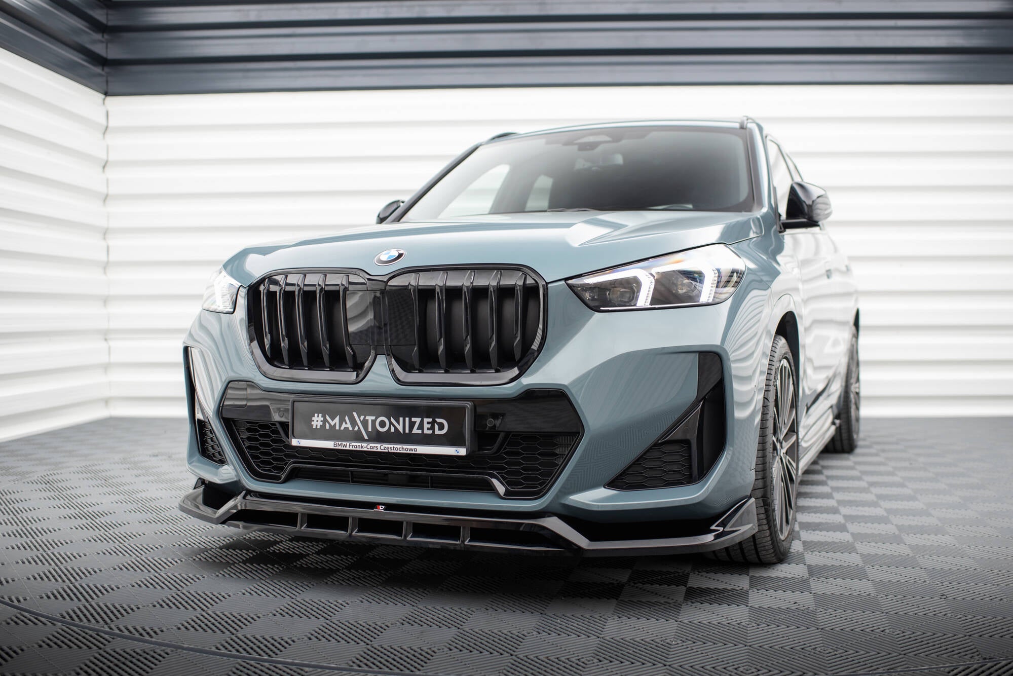 Frontspoiler BMW X1 M-Pakke U11 i lys blå metallic sett forfra fra venstre med sorte grilldetaljer.