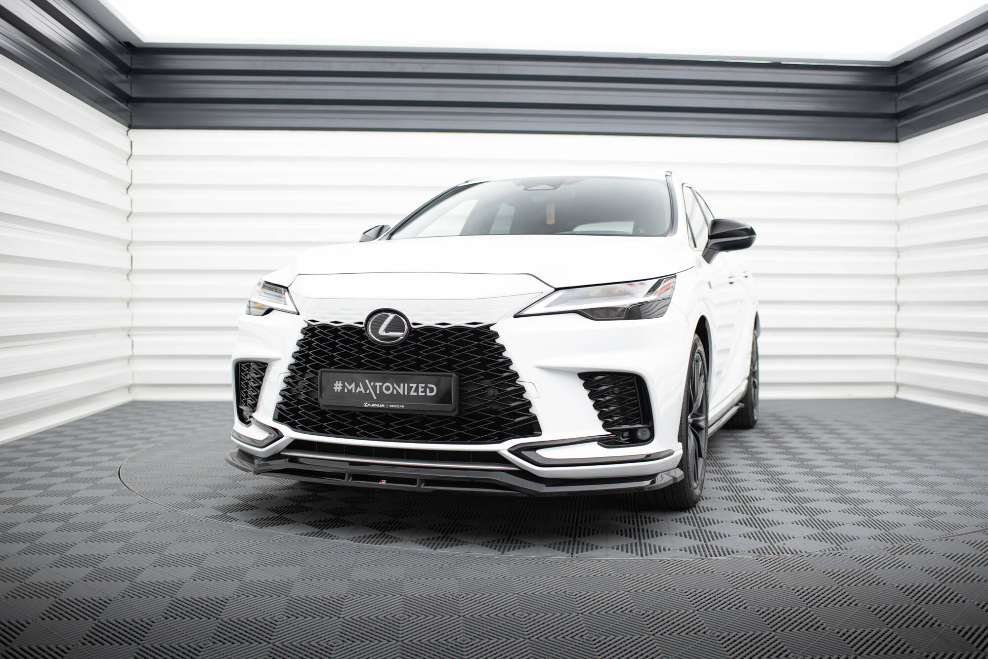 Frontspoiler på hvit Lexus RX F-Sport MK5 med sort grill og LED-frontlykter i lyst rom.