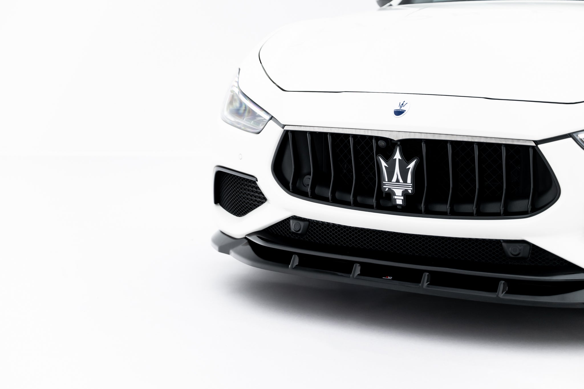 Front splitter på Maserati Ghibli Modena MK3 Facelift med sort grill og synlig logo mot hvit bakgrunn.