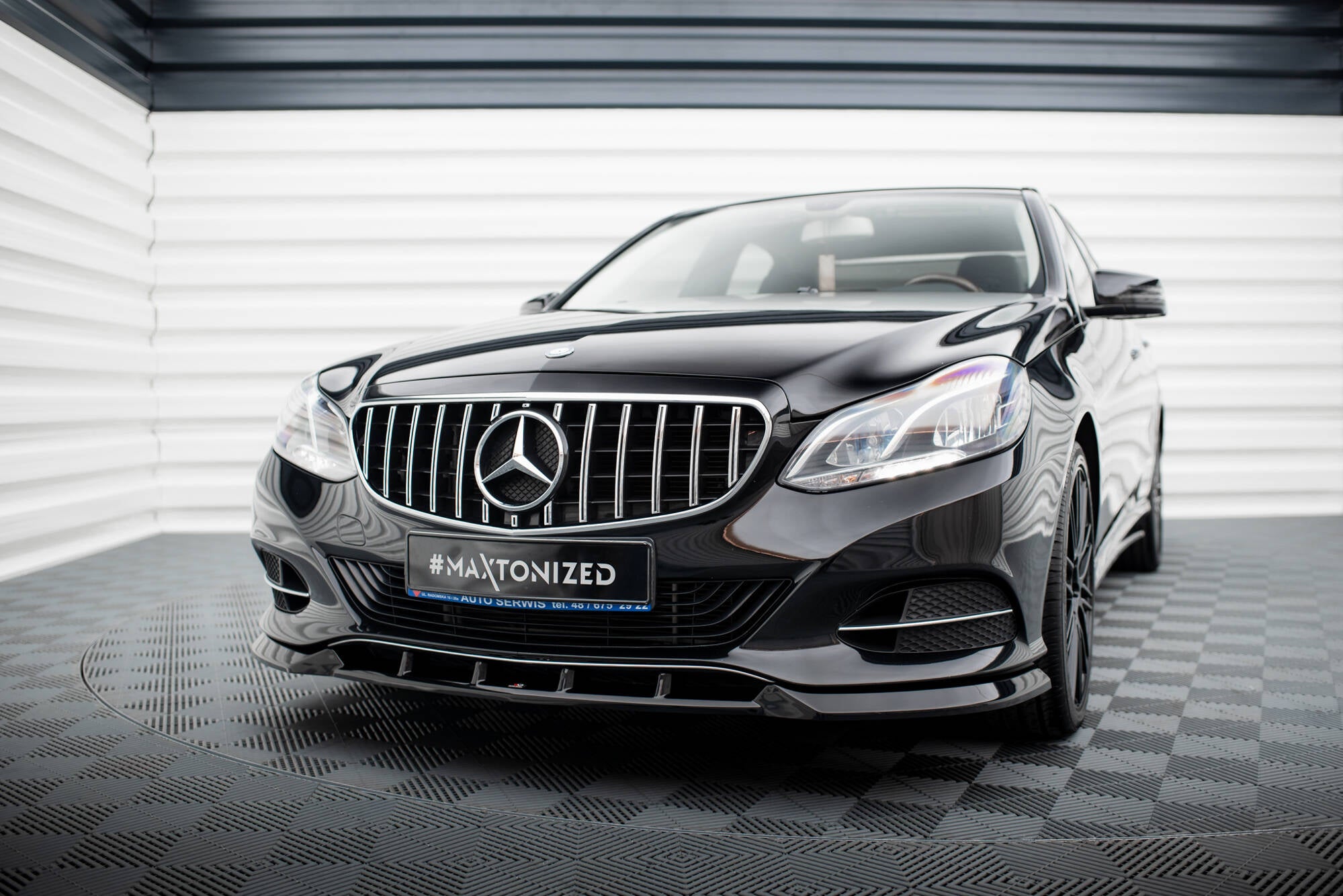 Frontspoiler Mercedes E W212 Facelift på sort bil i lyst showroom med kromgrill og LED-frontlykter.