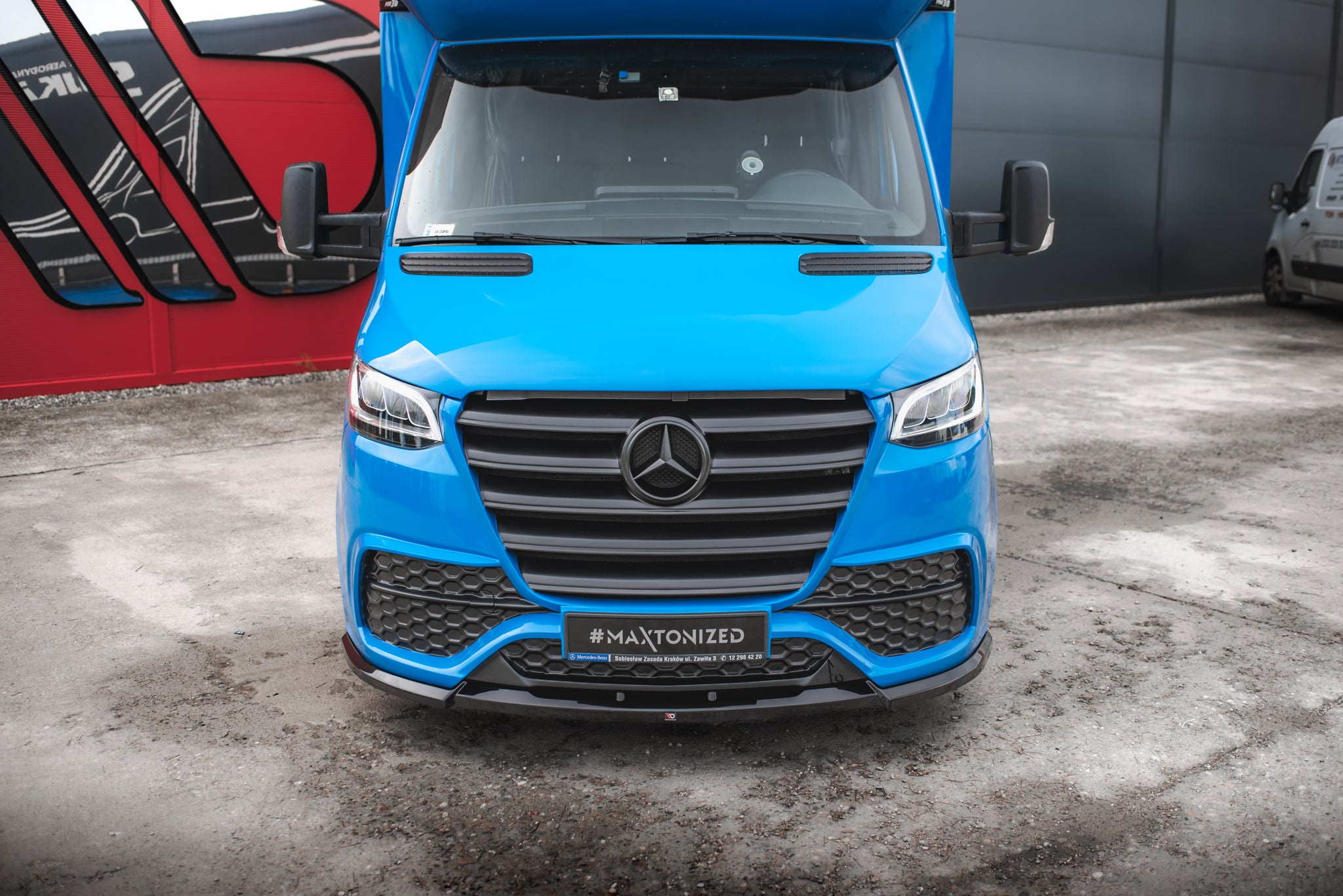 Frontspoiler på blå Mercedes Sprinter MK3 sett forfra med sort grill og synlig Mercedes-logo.
