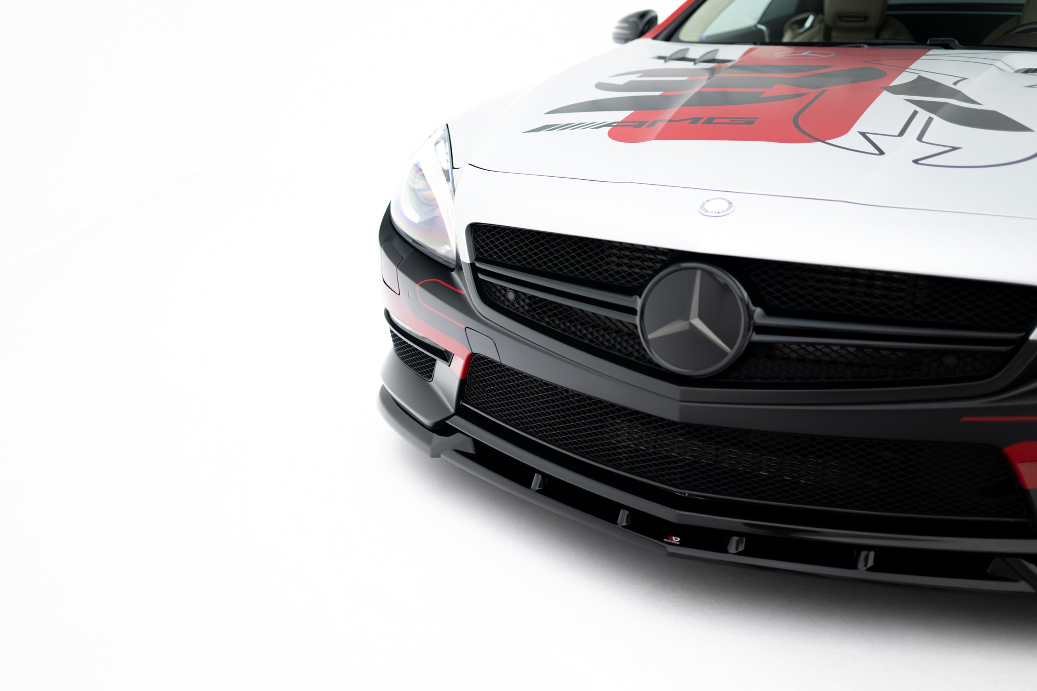 Spoiler på Mercedes SL 63 AMG R231 V.1 med sort grill, tydelig logo og rød-svart dekor mot hvit bakgrunn.