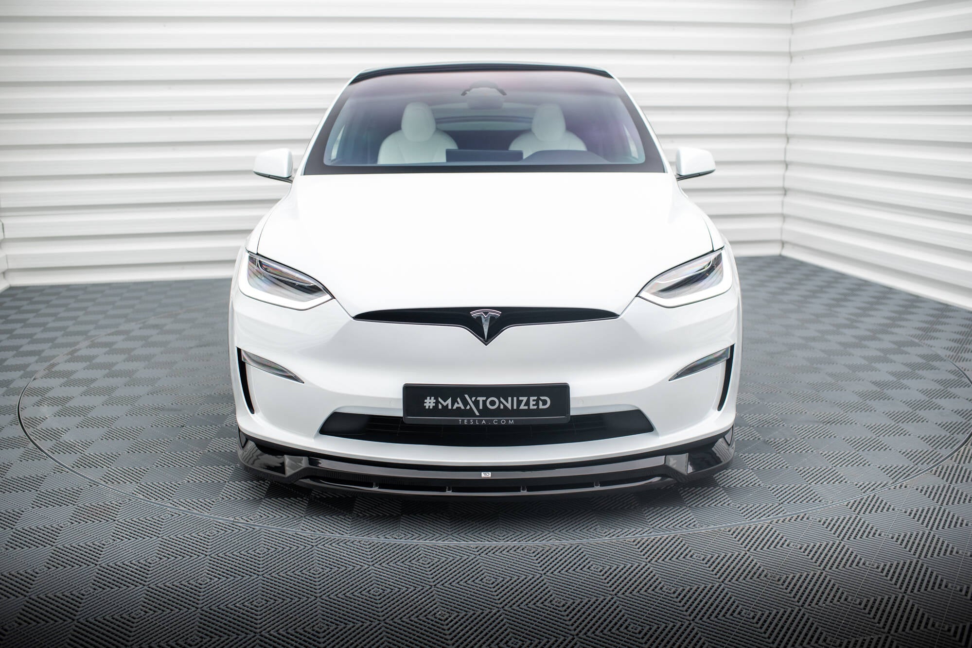 Frontleppe på Tesla Model X MK1 Facelift V.1, svart spoiler på hvit bil sett forfra innendørs.
