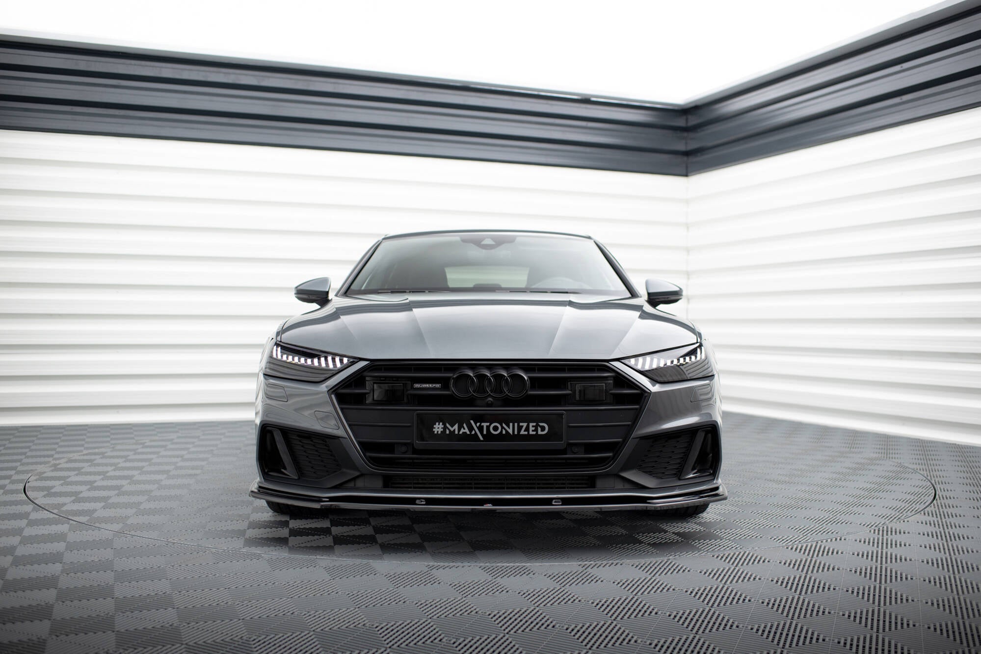 Frontleppe Audi A7 S-Line C8 med markante LED-lys og sort grill, fotografert forfra i lyst rom.