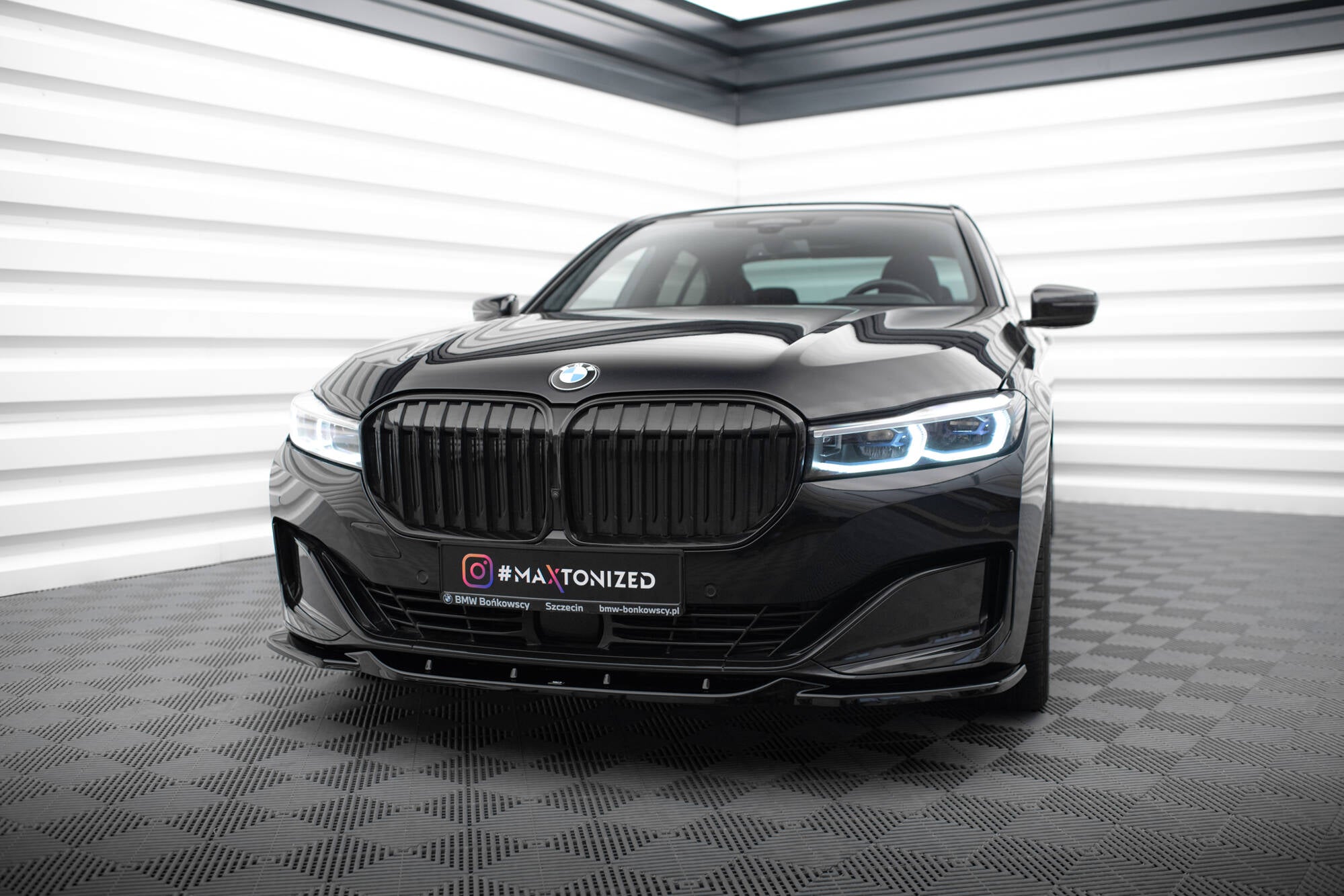 Frontspoiler BMW 7 G11/G12 Facelift V.2 montert på sort sedan sett forfra i lyst showroom.