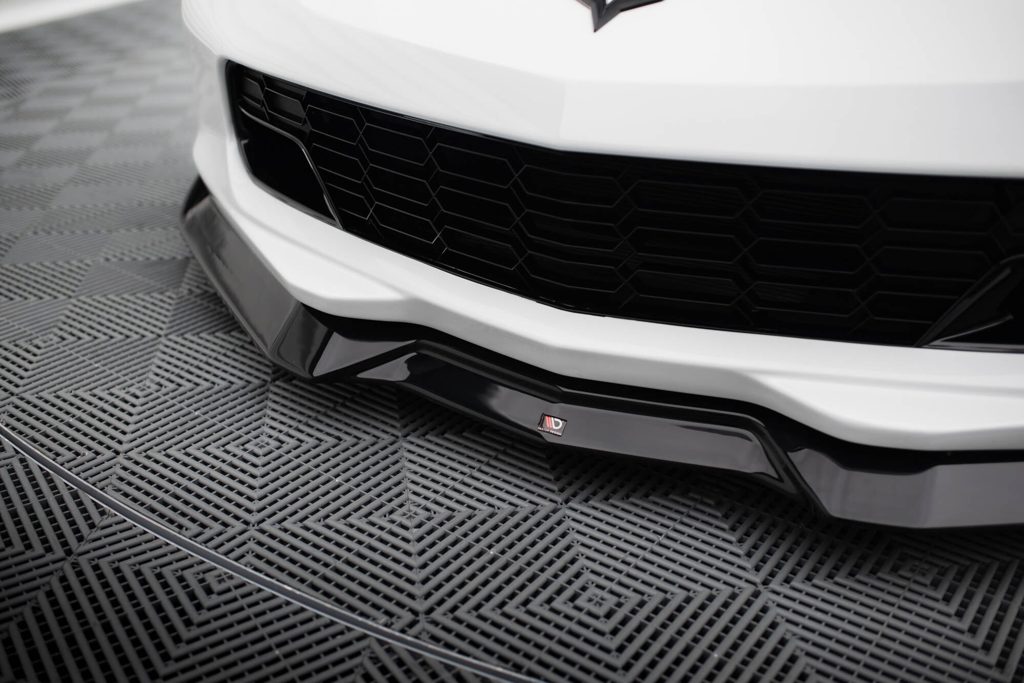 Spoiler til Chevrolet Corvette C7 V.2 i sort blank plast montert under hvit støtfanger med grill.