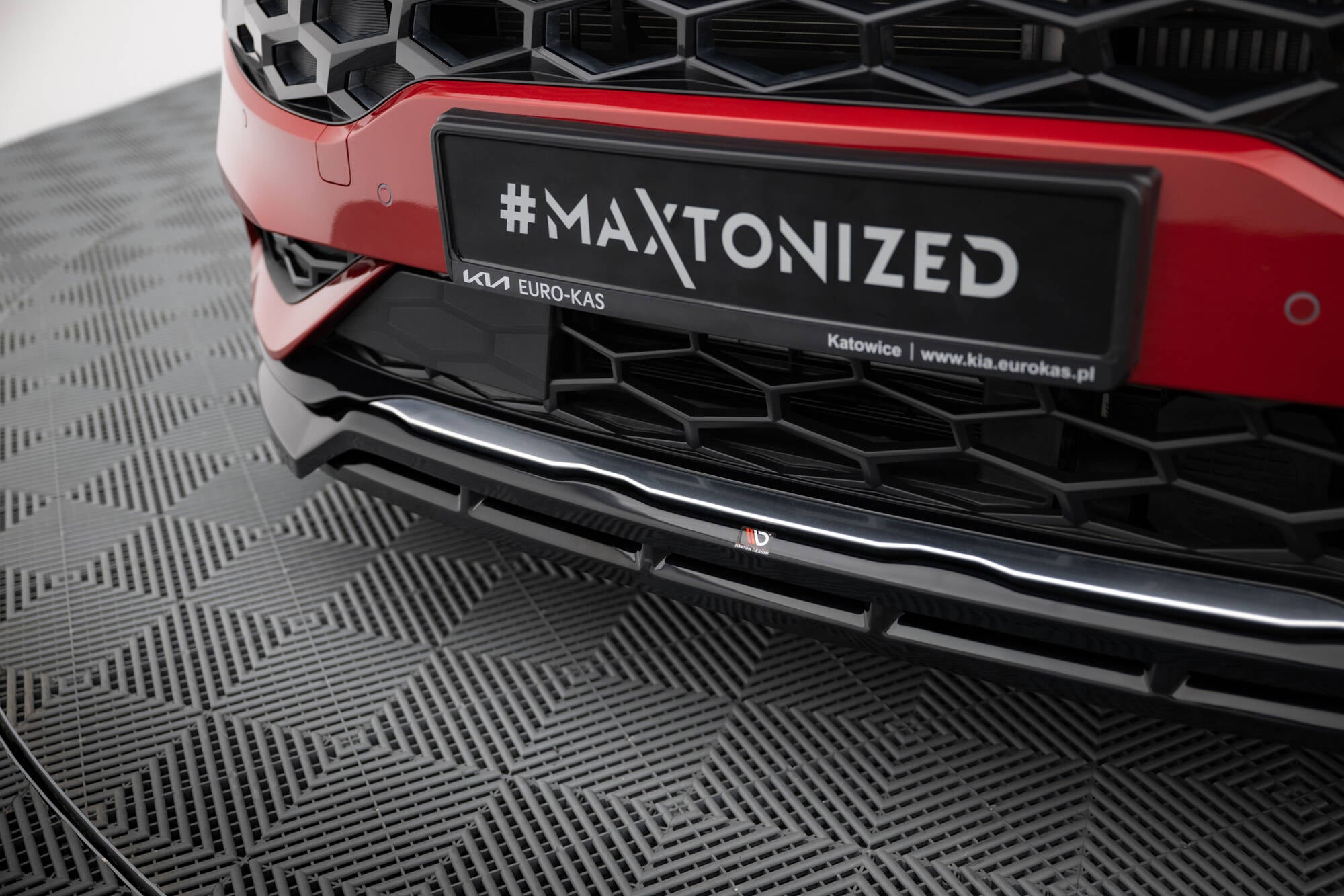 Spoiler Kia Sportage GT-Line MK5 V.2 med sort leppe og bikubemønstret grill under rød bilfront.