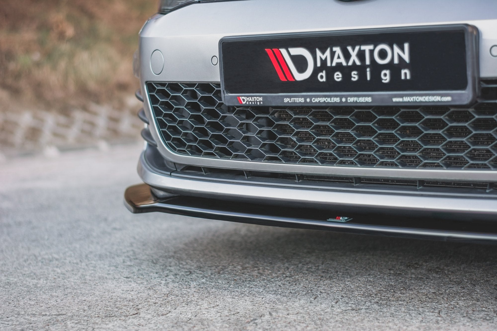 Spoiler til VW Golf 7 GTI V.2 med sort, blank frontsplitter og bikubemønstret grill, Maxton Design-logo.