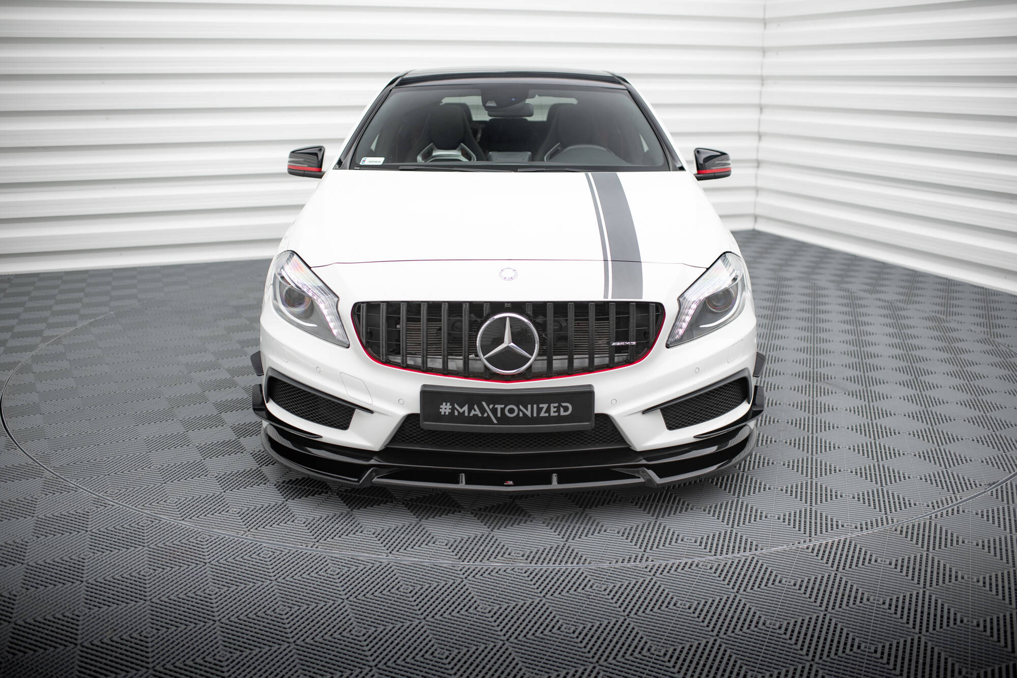 Frontleppe på Mercedes A45 AMG W176 med svart grill, røde detaljer og grå racingstripe på hvit bil.