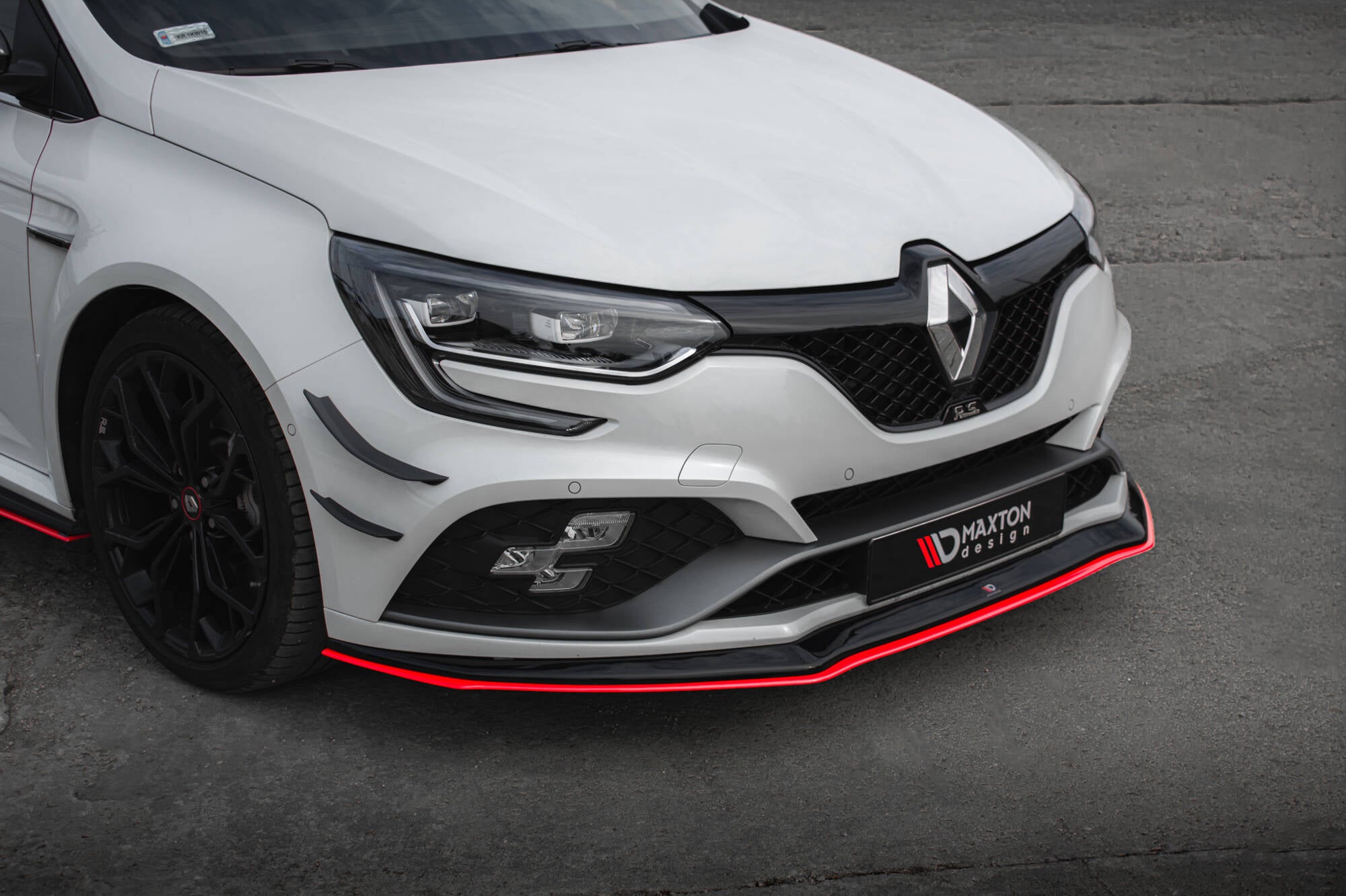 Frontspoiler Renault Megane RS MK4 V.3 med sort splitter og rød kant på hvit bil, sett fra venstre hjørne.