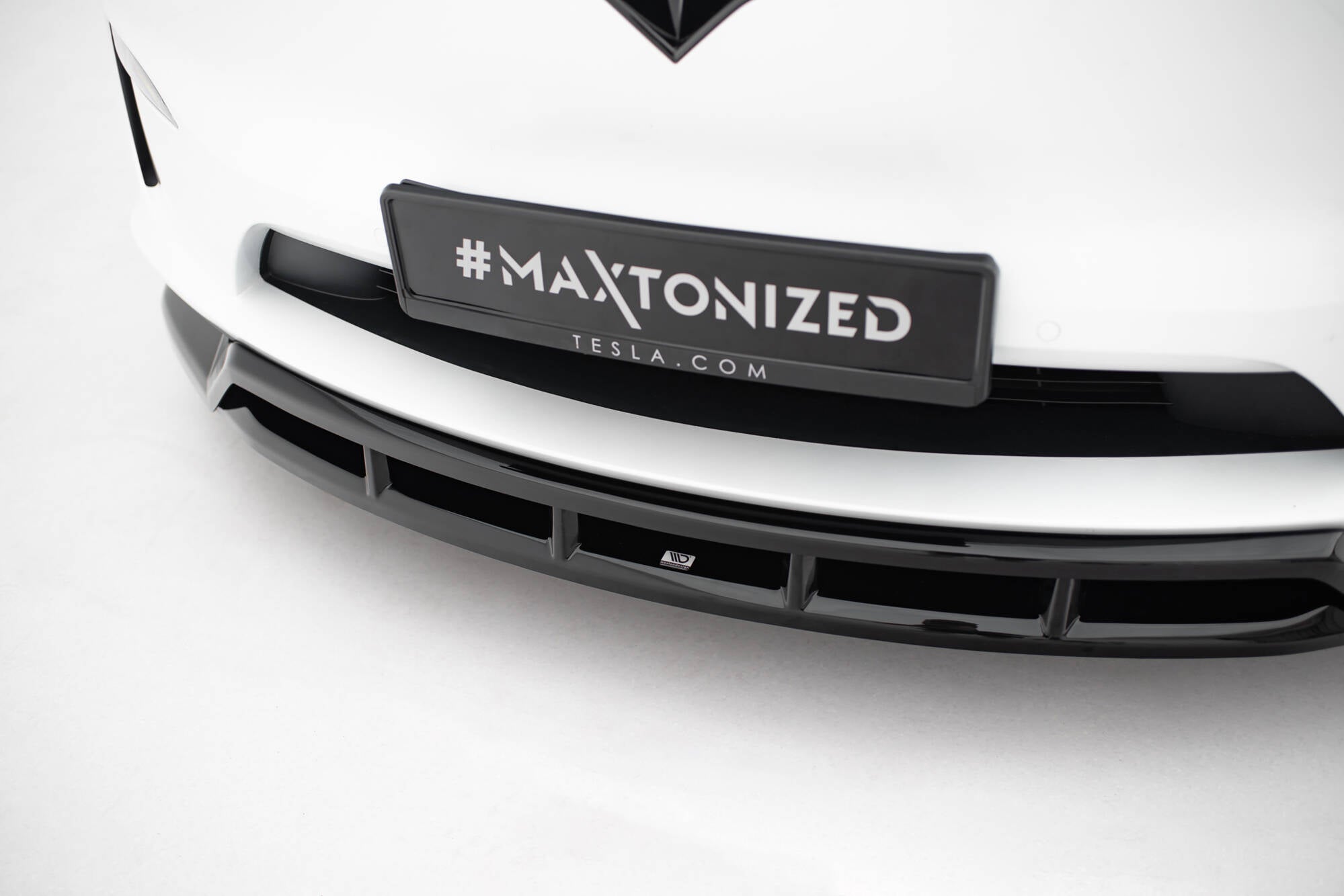 Front splitter på hvit Tesla Model X MK1 Facelift V.3 med sorte vertikale delinger og #MAXTONIZED-skilt.