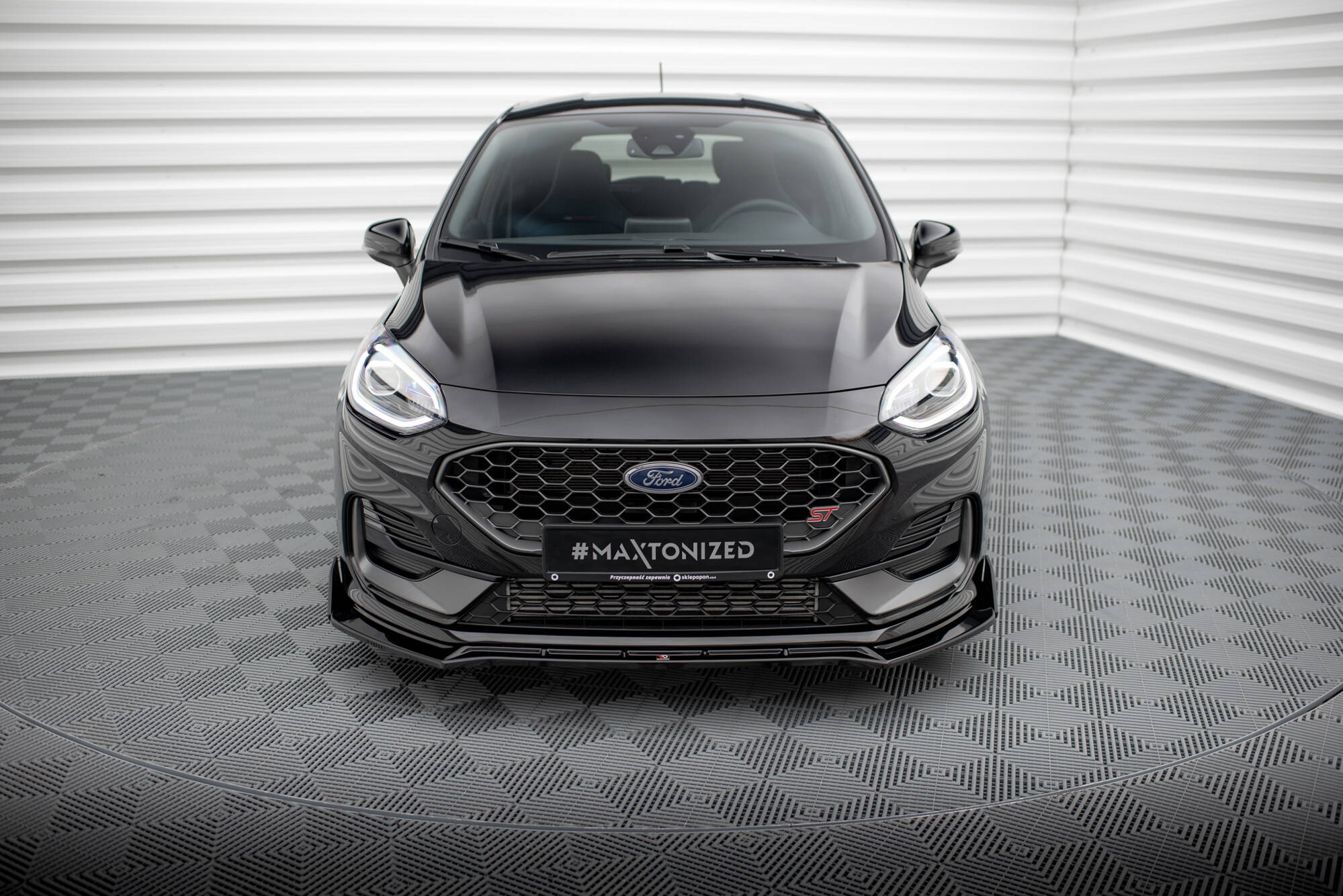 Front splitter på Ford Fiesta MK8 Facelift med sort grill, skarpe lykter og sportslig design i lyst rom.