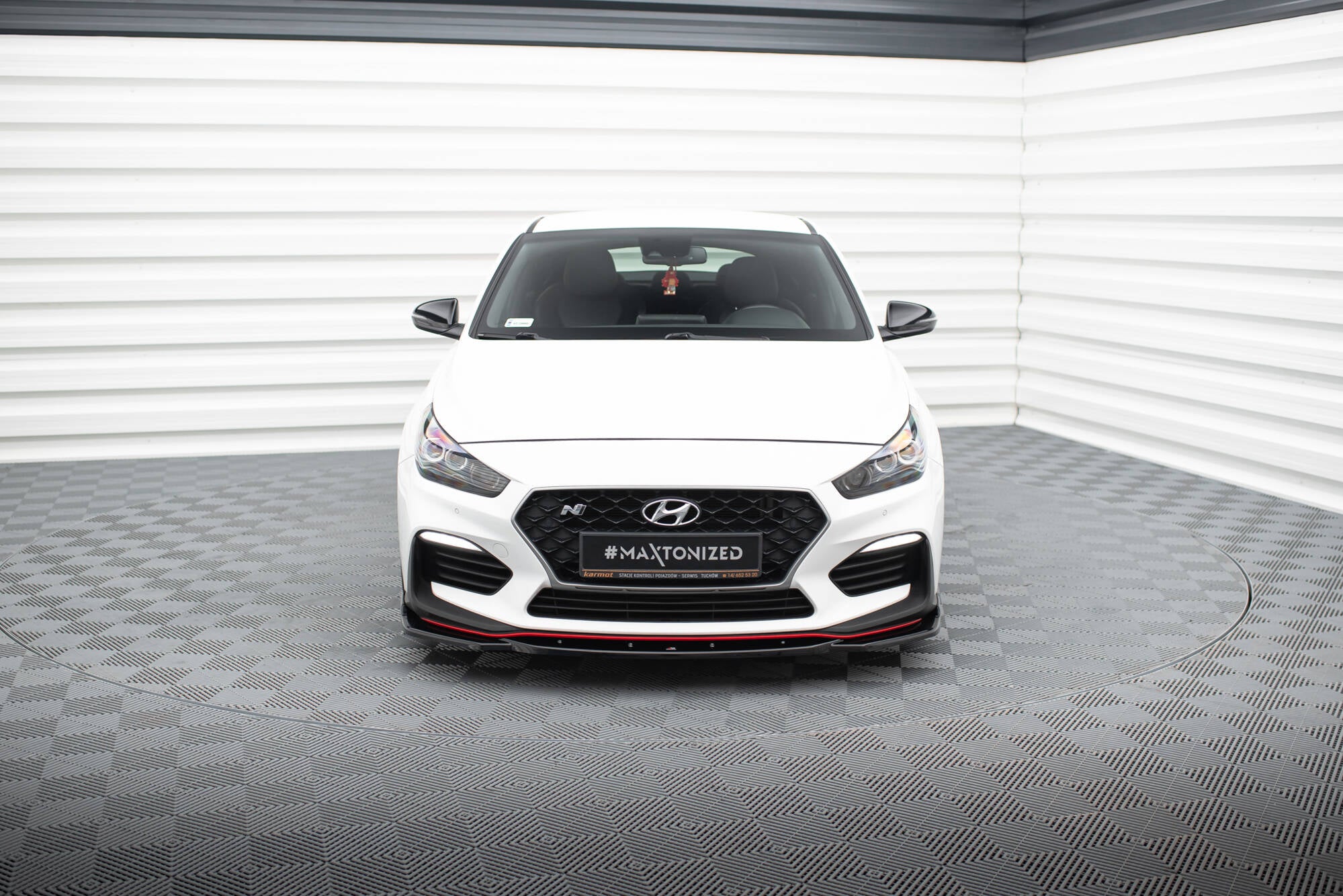 Frontleppe Hyundai I30 N MK3 hvit bil sett forfra med røde detaljer og sort grill i lyst rom.
