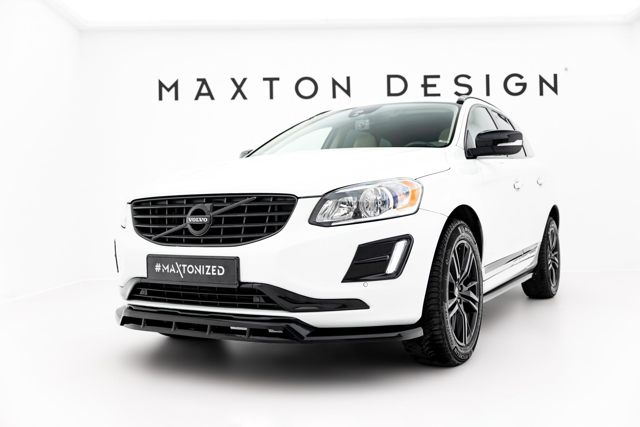 Frontleppe på hvit Volvo XC60 MK1 Facelift med sorte detaljer, fotografert skrått forfra i lyst studio.