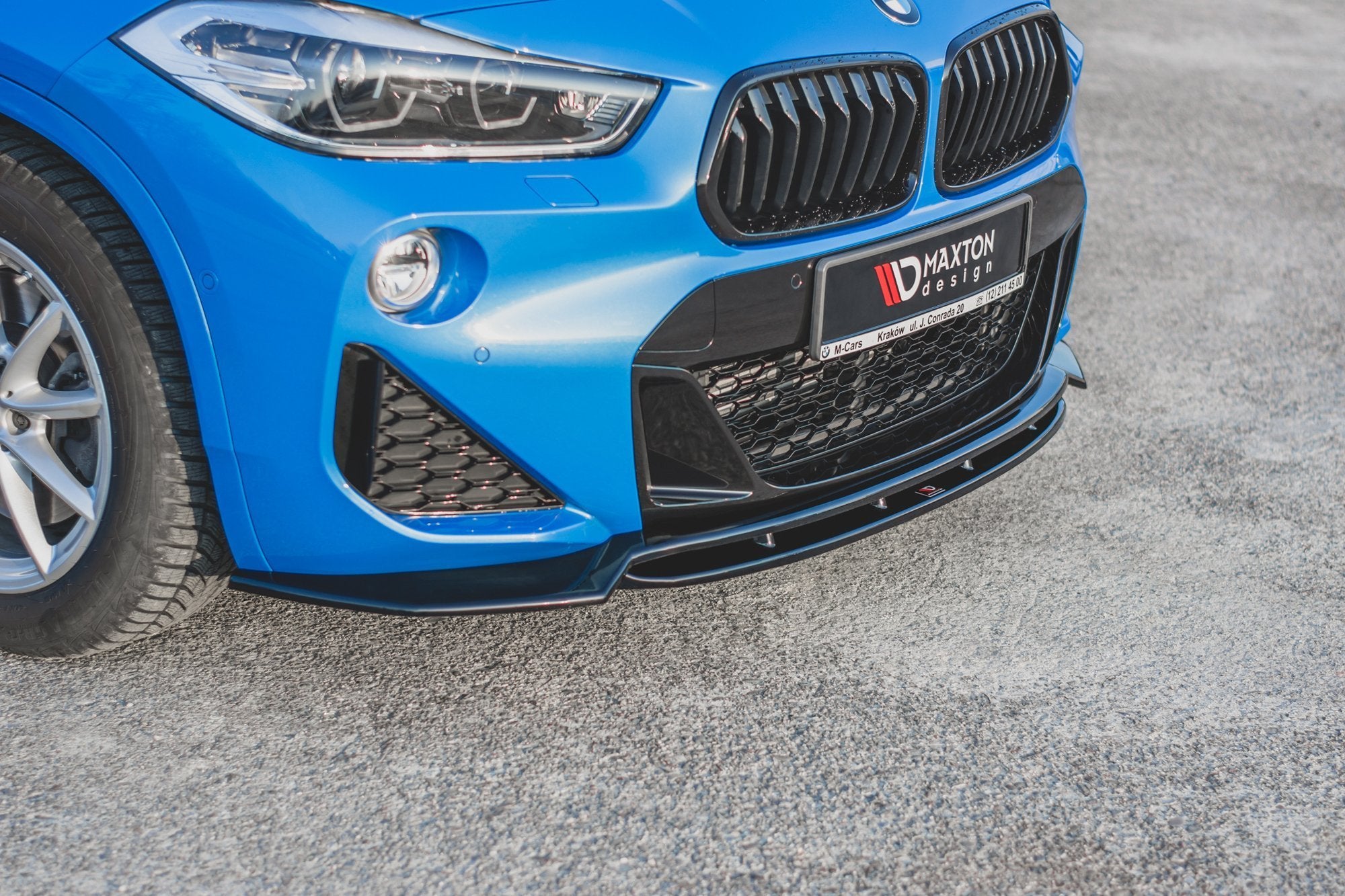 Spoiler til BMW X2 F39 M-Pakke, svart frontsplitter under grill og luftinntak, sett fra skrå vinkel.