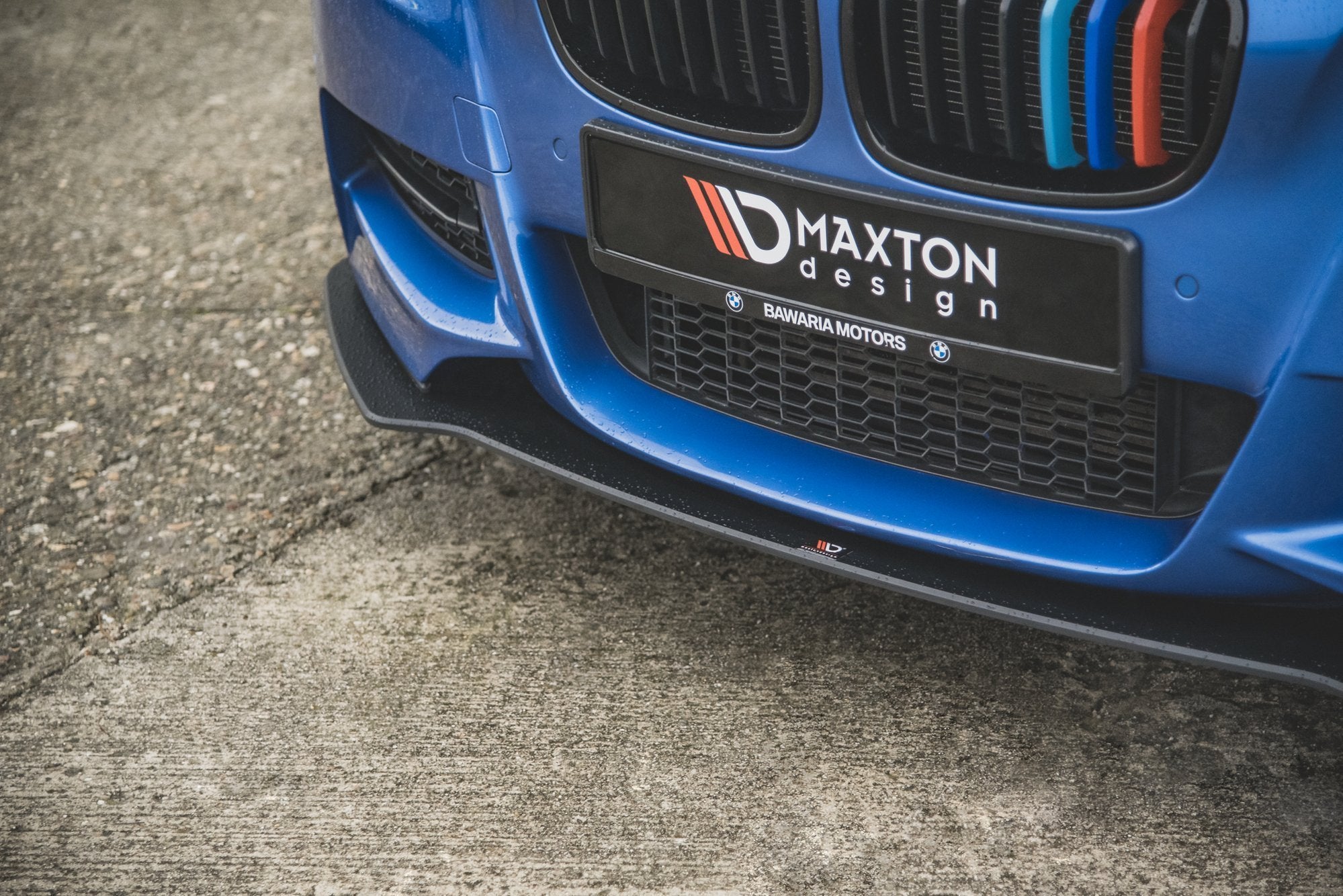 Front splitter på BMW M135I F20 med sort plast og Maxton Design-logo, sett fra skrå vinkel.
