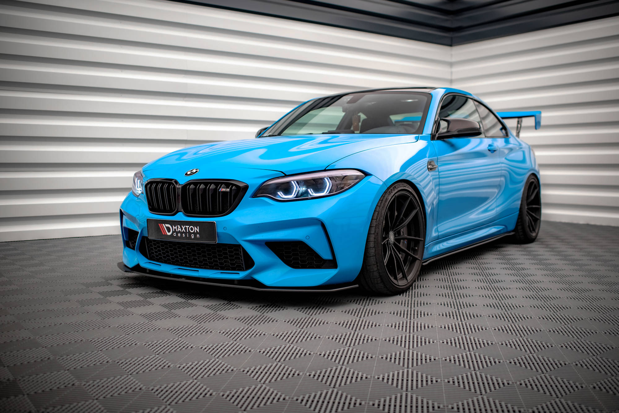 Spoiler på BMW M2 Competition F87 i blått med sorte felger og store luftinntak, innendørs miljø.