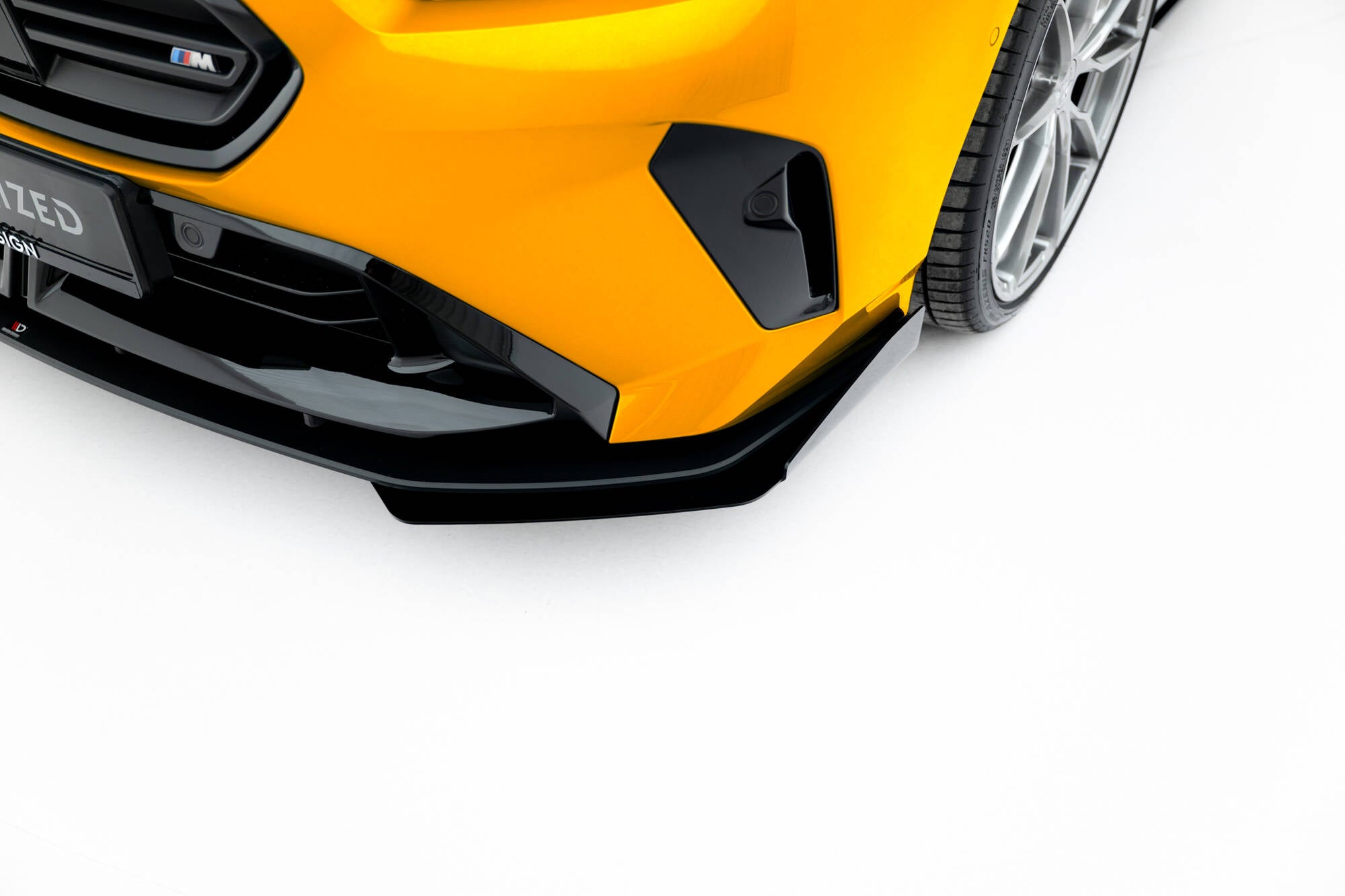 Front splitter på BMW F70 1 M-Pakke med flaps, nærbilde av gul bil med svarte detaljer og sølvfelg.