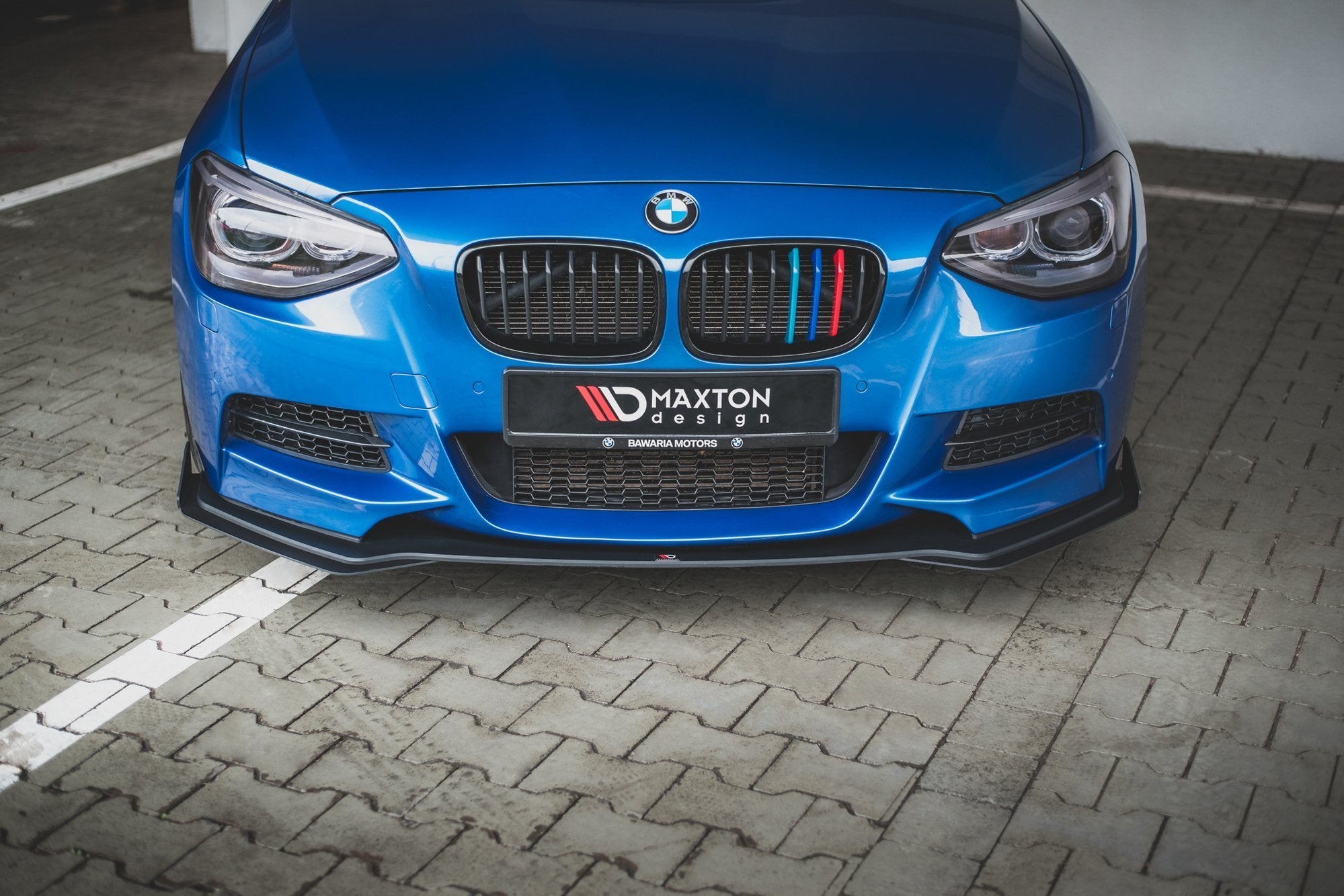 Frontspoiler på BMW M135I F20 2011, blå bil med sorte detaljer og fargede grillstriper.