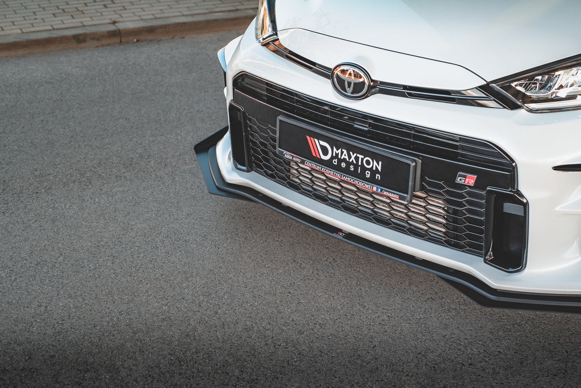 Front splitter på Toyota GR Yaris MK4 RS i sort plast med rillede detaljer, montert på hvit støtfanger.
