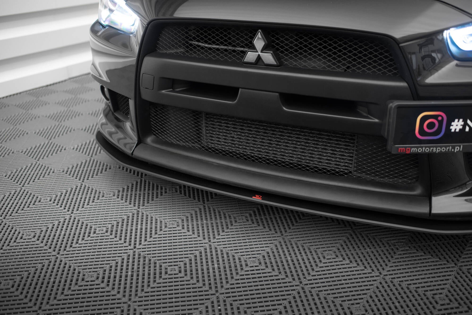 Spoiler til Mitsubishi Lancer Evo X Front V1 i sort med røde detaljer, sett forfra mot grått gulv.