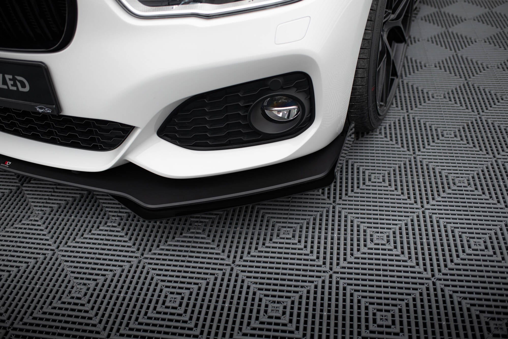 Front splitter på hvit BMW 1 F20 M-Pakke Facelift med sort luftinntak og ekstralys, sett skrått forfra.