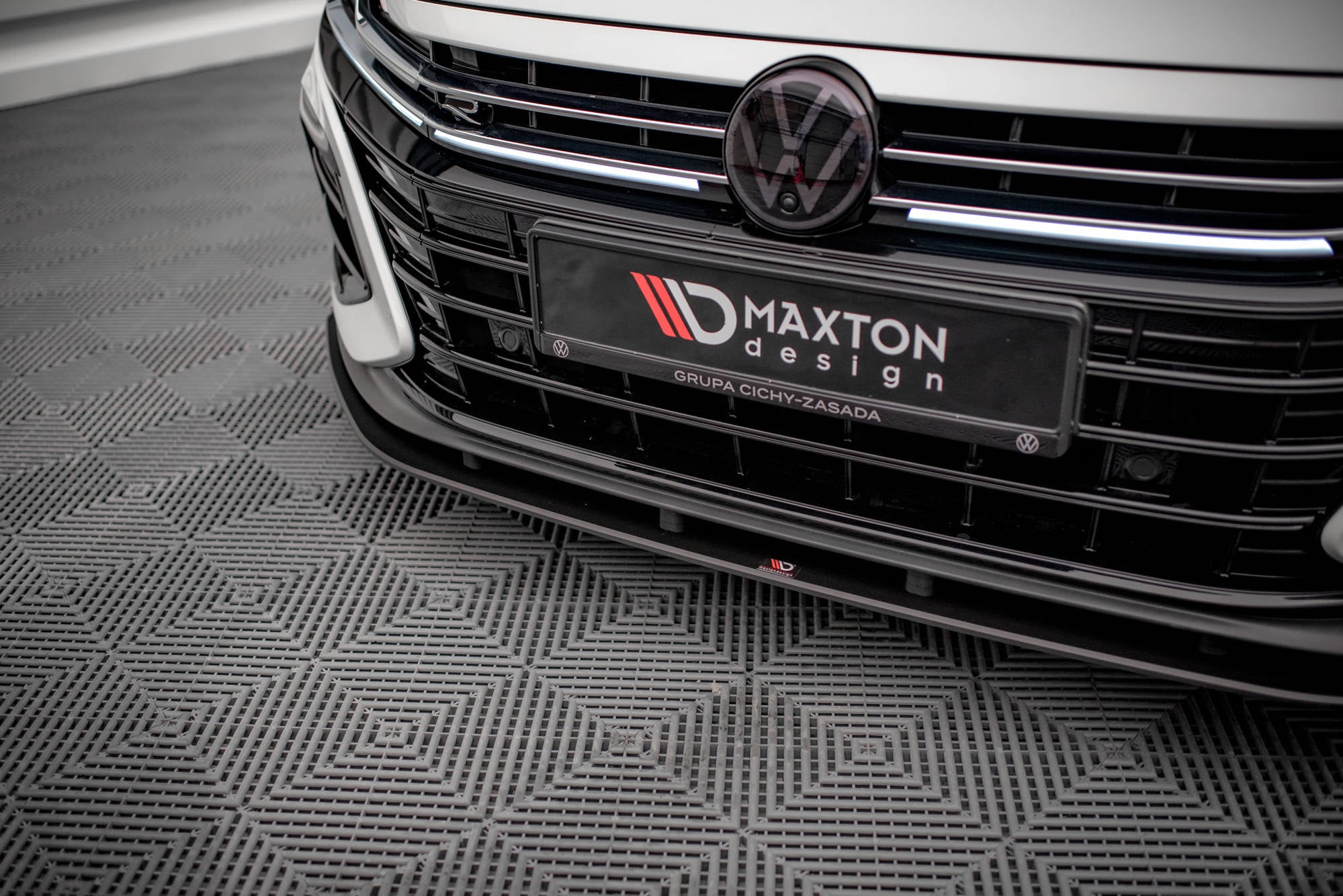 Spoiler til VW Arteon R med sort grill, Maxton Design-logo og mønstret gulv under bilen.