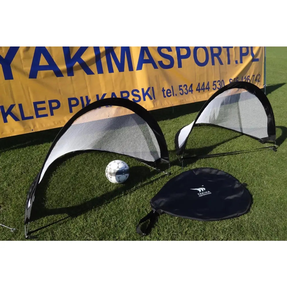 To pop-up fotballmål i sort og hvitt på gress, med bæreveske og fotball foran reklamebanner.