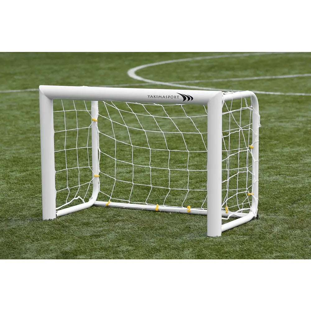 Port aluminium MINI PRO, lite hvitt fotballmål i plast med netting, skrå forside på kunstgress med banemerking.