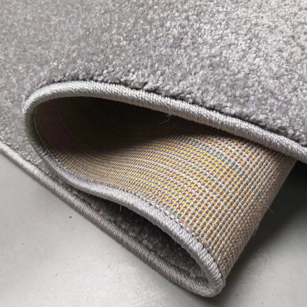 Portofino grått teppe, nærbilde av oppbrettet kant som viser vevd bakside og forsterket kant.