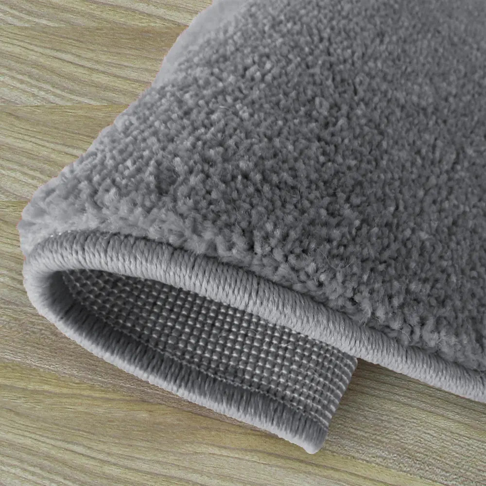 Portofino rundt teppe i grått, detaljnærbilde som viser lodden overside og rutete underside på lyst tregulv.