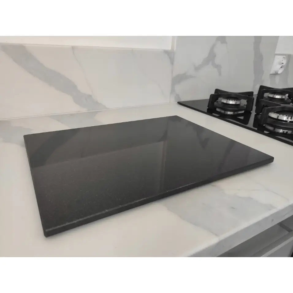 Premium svart granitt skjærebrett 30x40cm, sideprofil på lys benk med gassbluss i bakgrunnen.