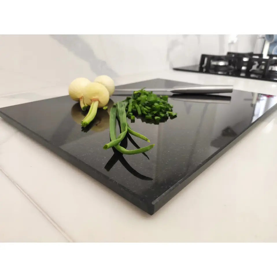 Premium svart granitt skjærebrett 30x40cm, sideprofil med urter, kniv og løk på hvit benkeplate.