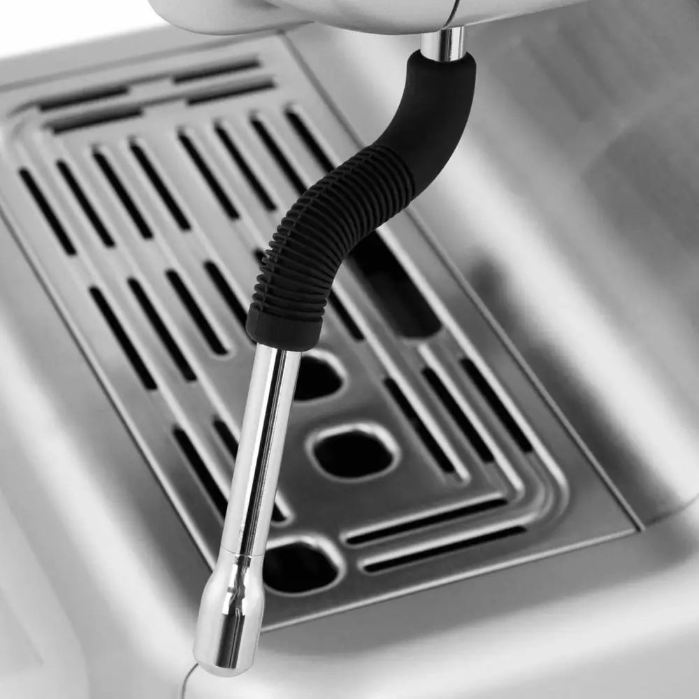 Damprør i rustfritt stål med sort riflet grep, detaljert over metallisk rillet dryppbrett på kaffemaskin.