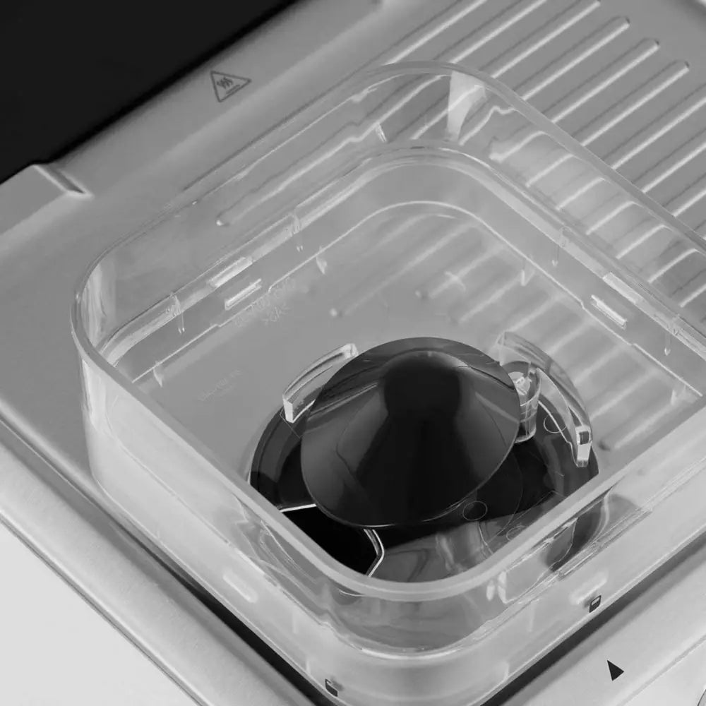 Gjennomsiktig beholder med svart sitruspresse sett ovenfra, plassert på rillemønstret metallunderlag.